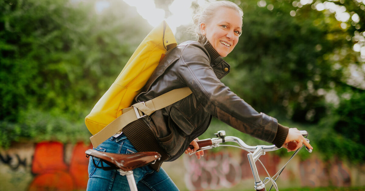 Eine Frau mit gelben Rucksack steigt auf ihr Fahrrad.